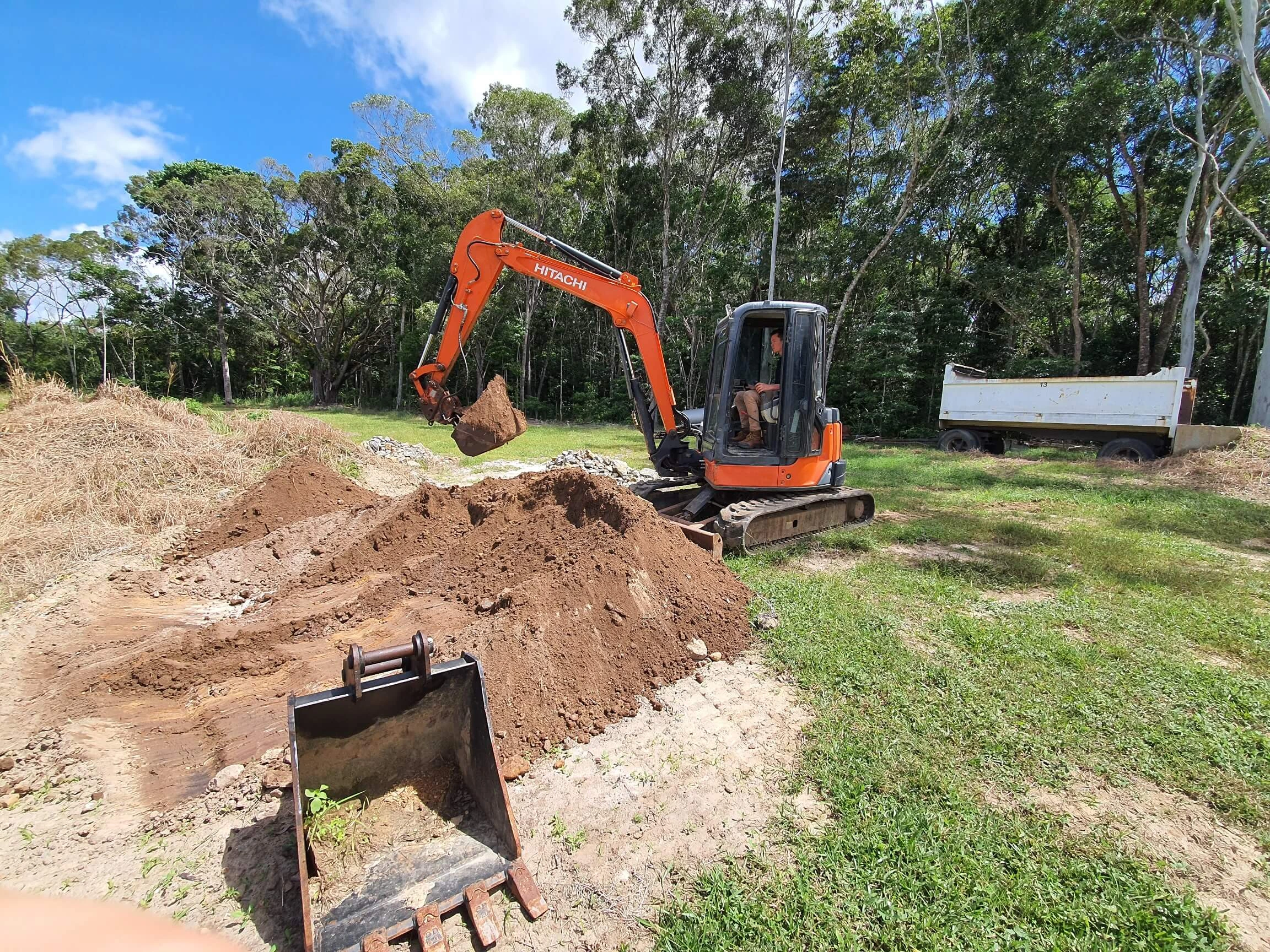 An orange excavator digs into a pile of dirt